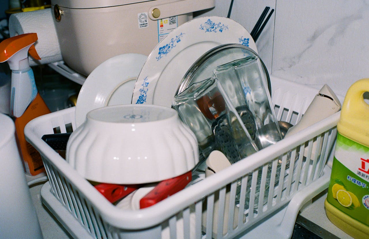 Clean kitchenware including plates and glasses drying in a dish rack with cleaning supplies nearby.