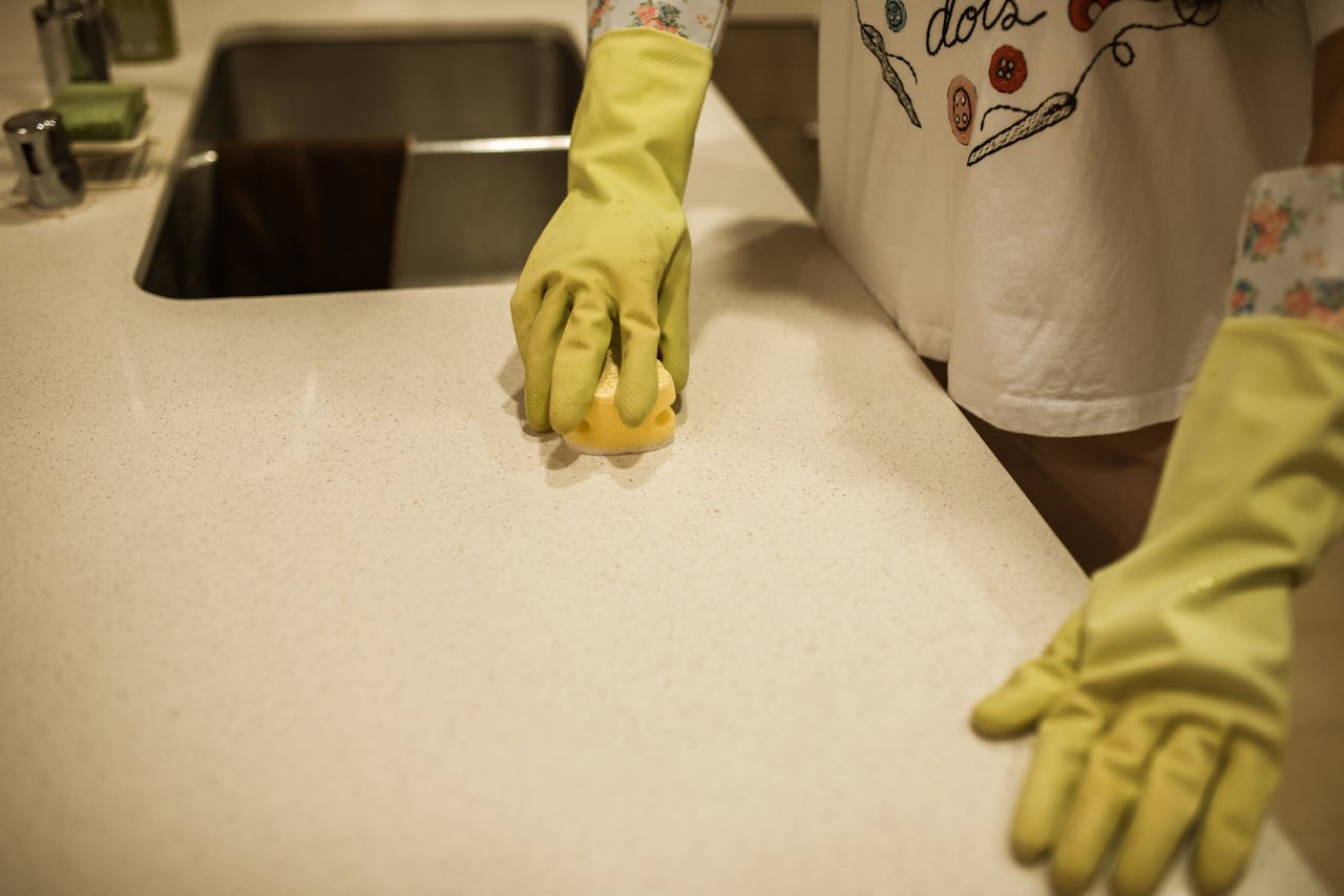 Woman using yellow rubber gloves to clean a kitchen counter with a sponge.